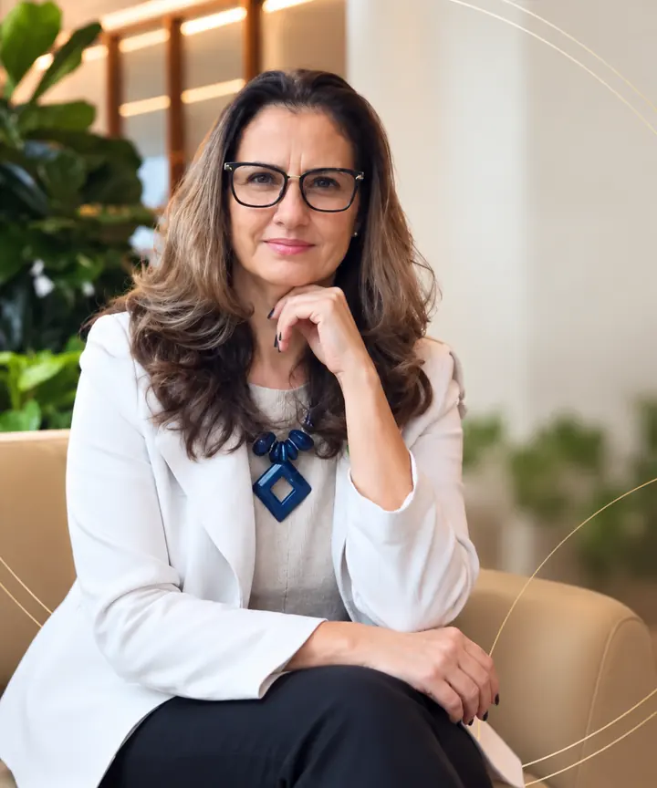 Luinni Forghieri de blazer branco e óculos, sentada, com a mão no queixo
